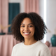 Portrait of a smiling young adult woman with dark, curly hair, looking trustworthy and happy.