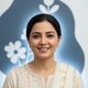 Portrait of a smiling Pakistani woman, mid-30s, against a soft slate blue and white background, exuding trust and happiness.